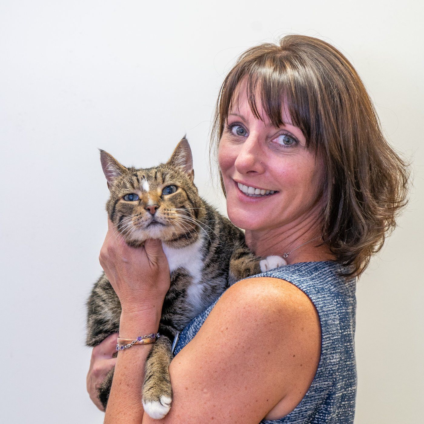 Woman holding a tabby cat, both facing the camera, against a plain background.